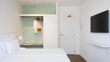 Una habitación de hotel con cama, armario, tocador con espejo y televisor montado en la pared.