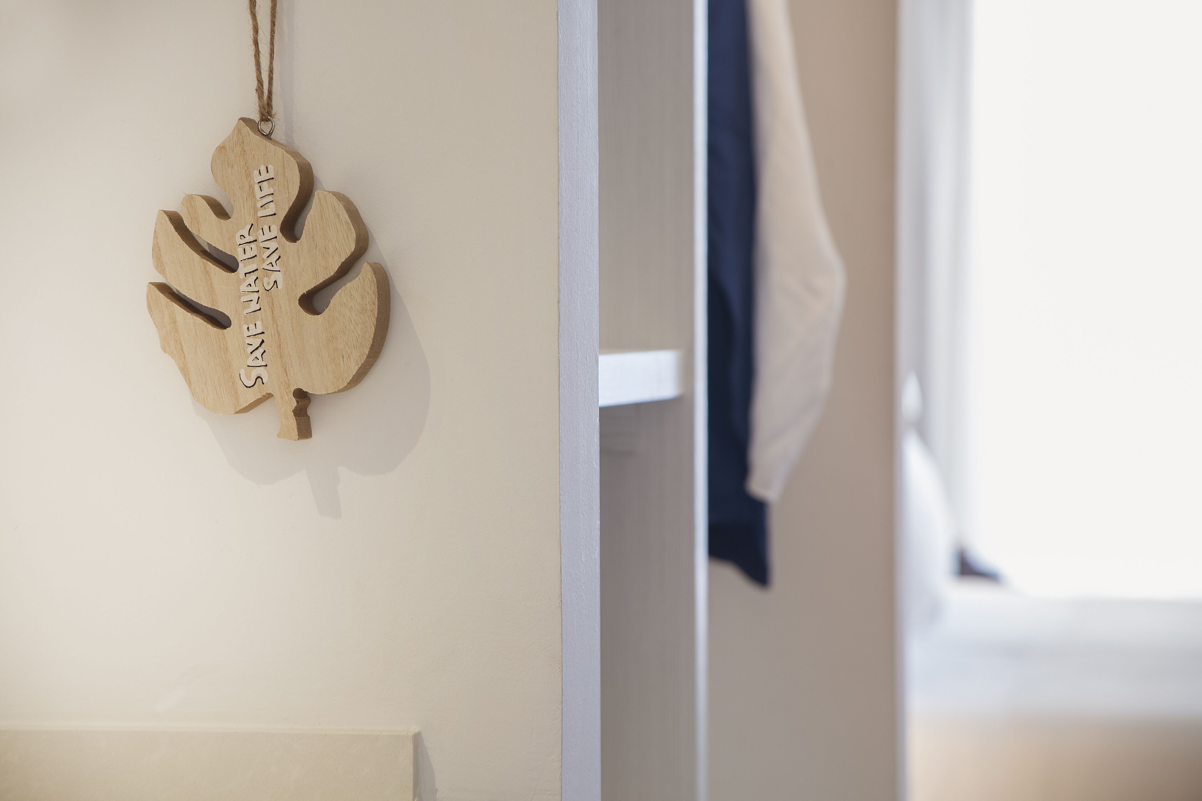 A wooden wall hanging with the text "SINE LABE" and a partial view of a room with a white door and a blue curtain.