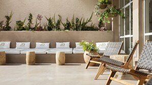 A sunlit outdoor seating area with cushioned benches, wicker chairs, and potted plants. - The 15th Boutique Hotel (Lloret de Mar)