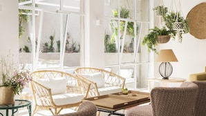 A bright room with large windows, wicker furniture, and hanging plants. - The 15th Boutique Hotel (Lloret de Mar)
