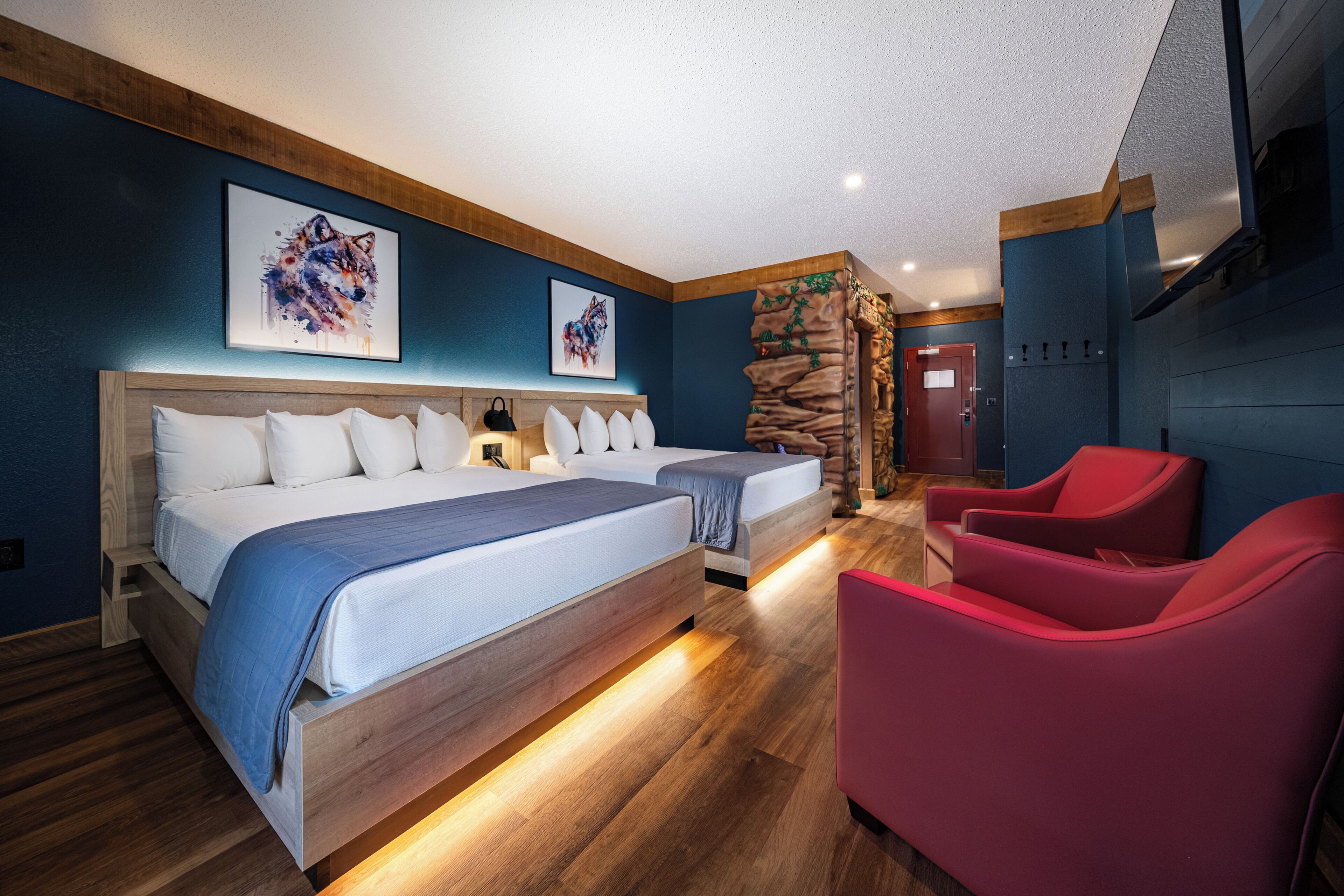 A hotel room with a large bed, two smaller beds, a red chair, and a stone wall.