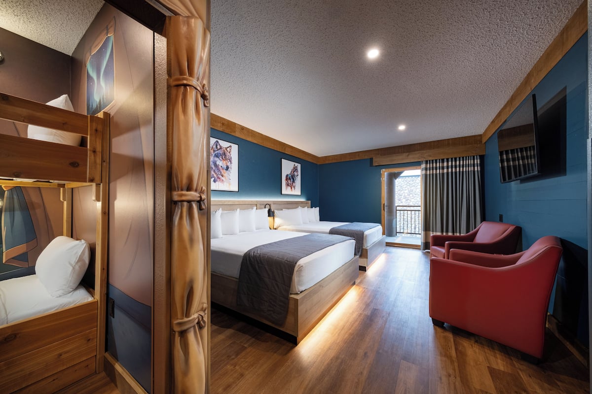 A room with a bunk bed, a single bed, a red chair, and a large window with curtains.