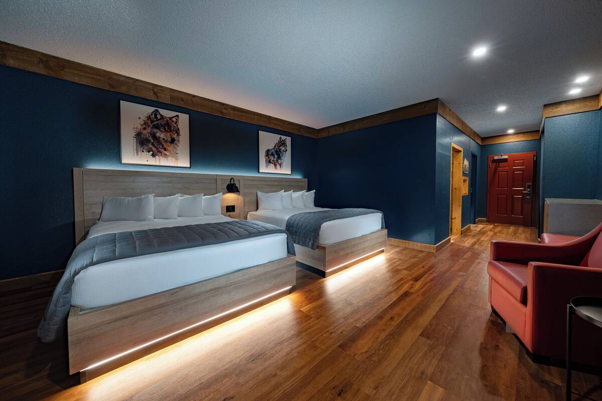 A hotel room with two beds, wooden flooring, and artwork on the walls.
