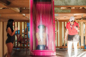 Une personne se trouve à l’intérieur d’une structure cylindrique transparente à l’extérieur rose, à côté d’une chaise rouge et d’un mur en bois.