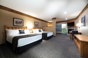 A hotel room with two beds, a TV, a desk, and a fireplace.