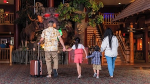 A family walking through a lobby with a large tree sculpture and a stone wall. - Great Wolf Lodge Niagara Falls (Niagara Falls)