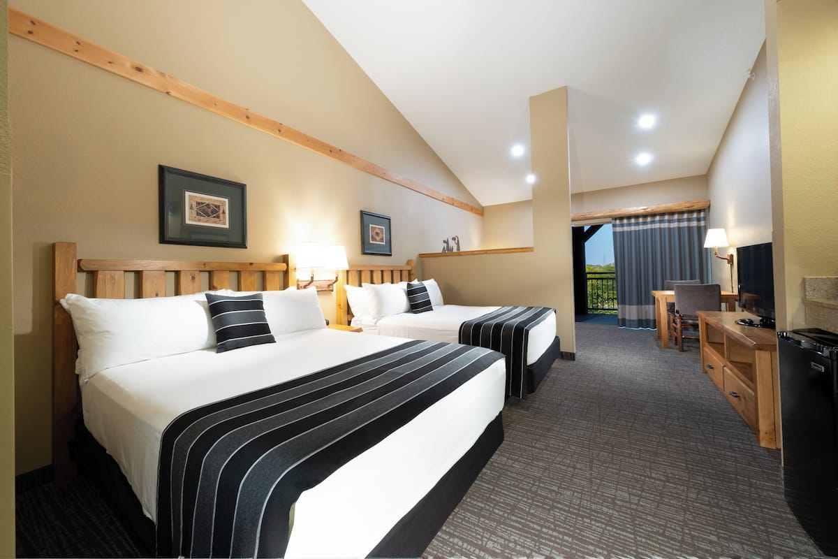 A hotel room with two beds, a desk, a chair, a television, and a balcony with curtains.