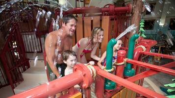 A water play area with red and green pipes, a wooden structure, and a sign indicating a return to the outdoor pool.