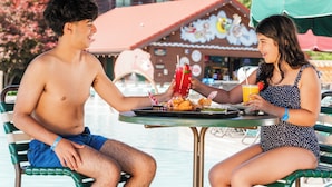 Two people sitting at a table with food and drinks, outdoors with a building in the background. - Great Wolf Lodge Niagara Falls (Niagara Falls)