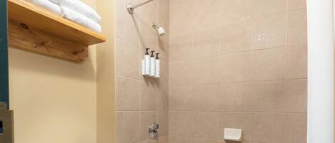 A bathroom with a toilet, bathtub, shower curtain, and a shelf with towels.
