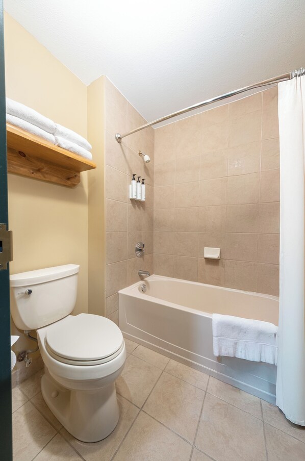 Un baño con inodoro, bañera, cortina de ducha y un estante con toallas.
