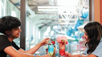 Deux personnes sont assises à une table, devant des boissons, dans un espace intérieur bien éclairé et doté de grandes fenêtres.