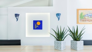 Un interior moderno con una obra enmarcadas, dos plantas en macetas y un diseño minimalista.