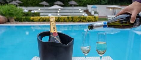 Une bouteille de champagne est versée dans un verre, le tout se déroulant au bord d’une piscine.