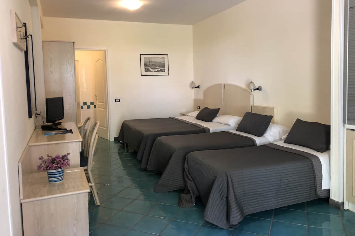 A hotel room with two beds, a desk with a computer, a chair, and a small table with a vase.