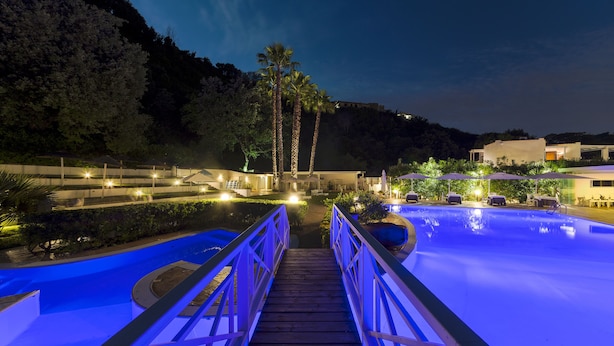 Un puente de madera que conduce a una zona de piscina con vistas a palmeras y un edificio al fondo.