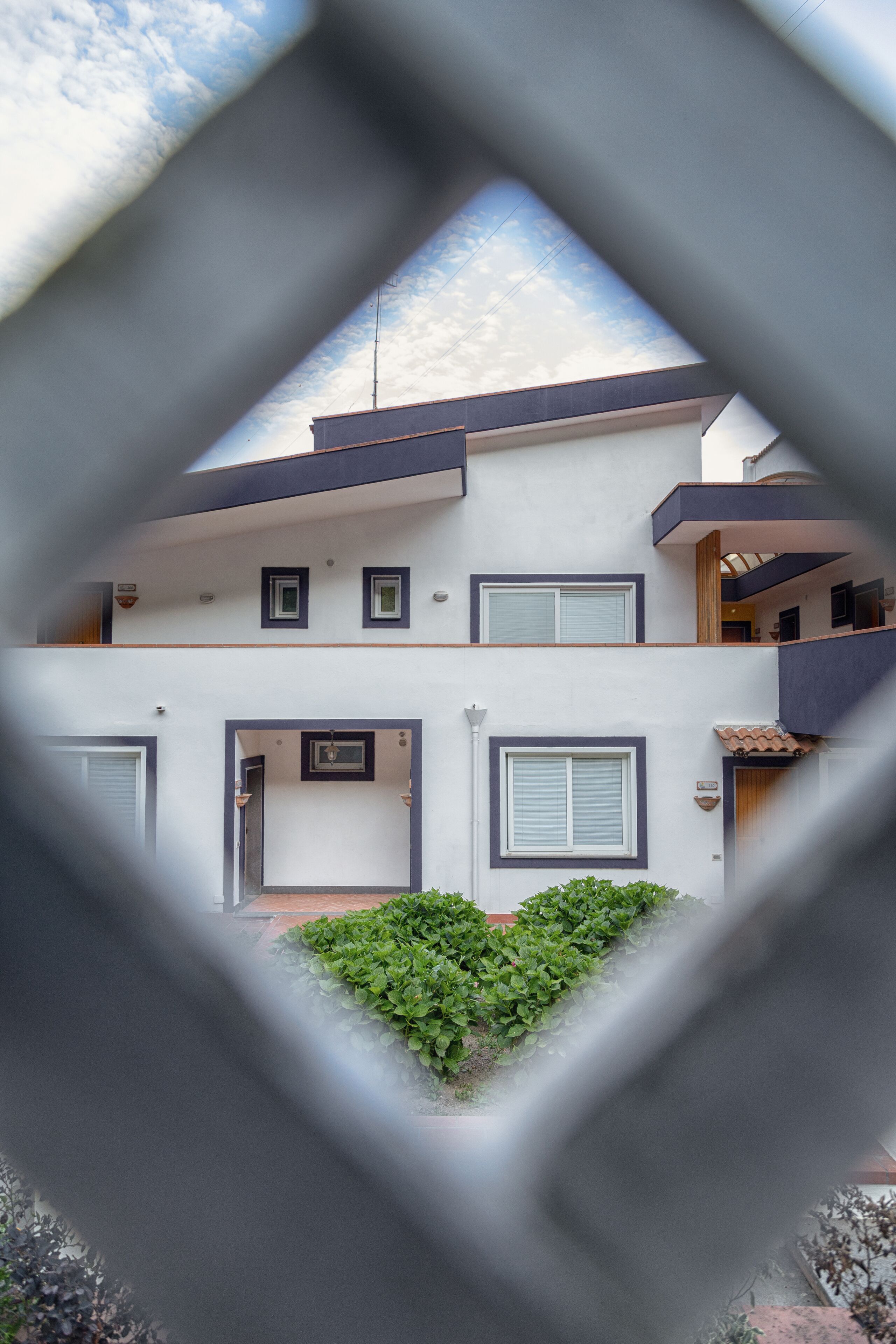 Un bâtiment moderne à deux étages, doté d’un balcon à l’étage supérieur, d’un petit jardin et d’une porte bien visible.