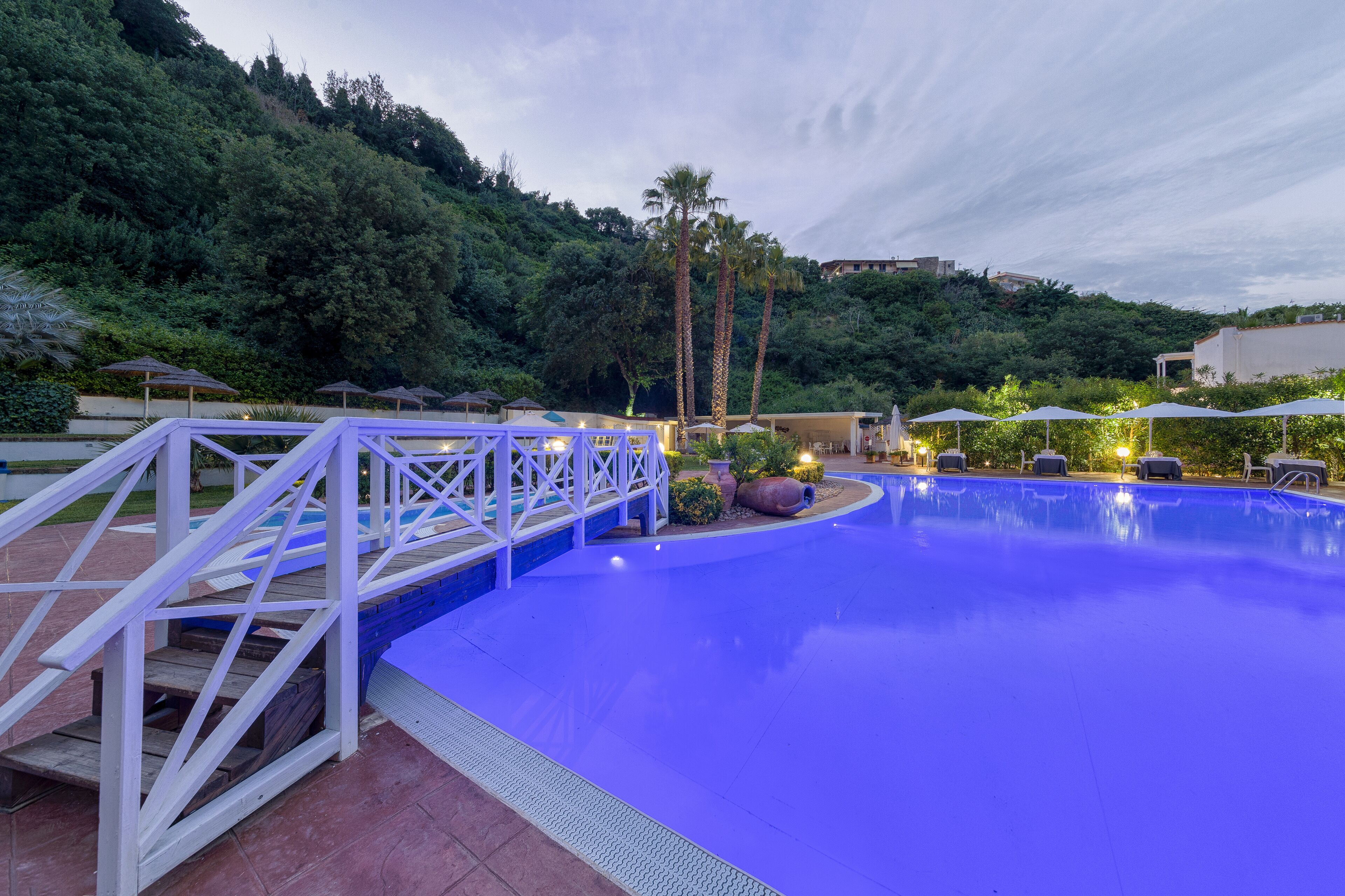 A swimming pool with a white deck and palm trees in the background.