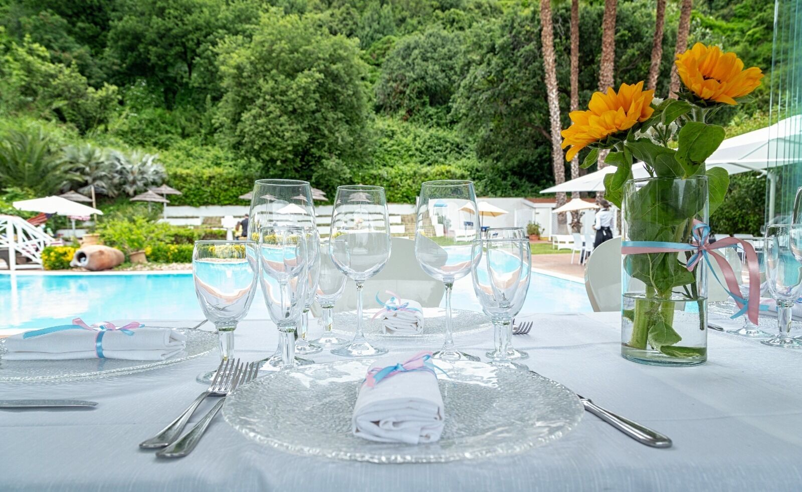 Una mesa dispuesta para una comida, con cristalería transparente, un mantel doblado y un florero con flores.