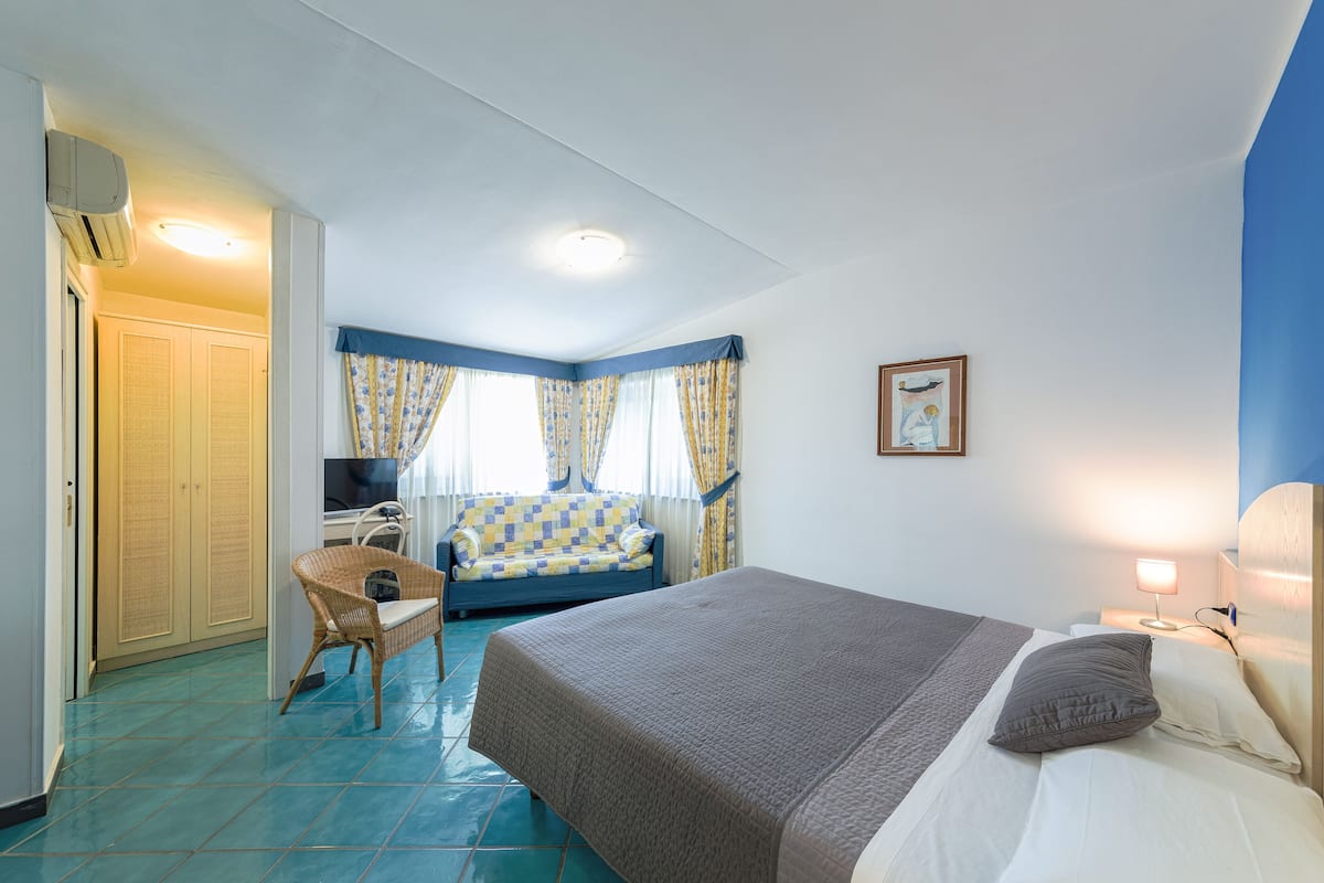 A bedroom with a bed, a chair, a desk, and a window with curtains.