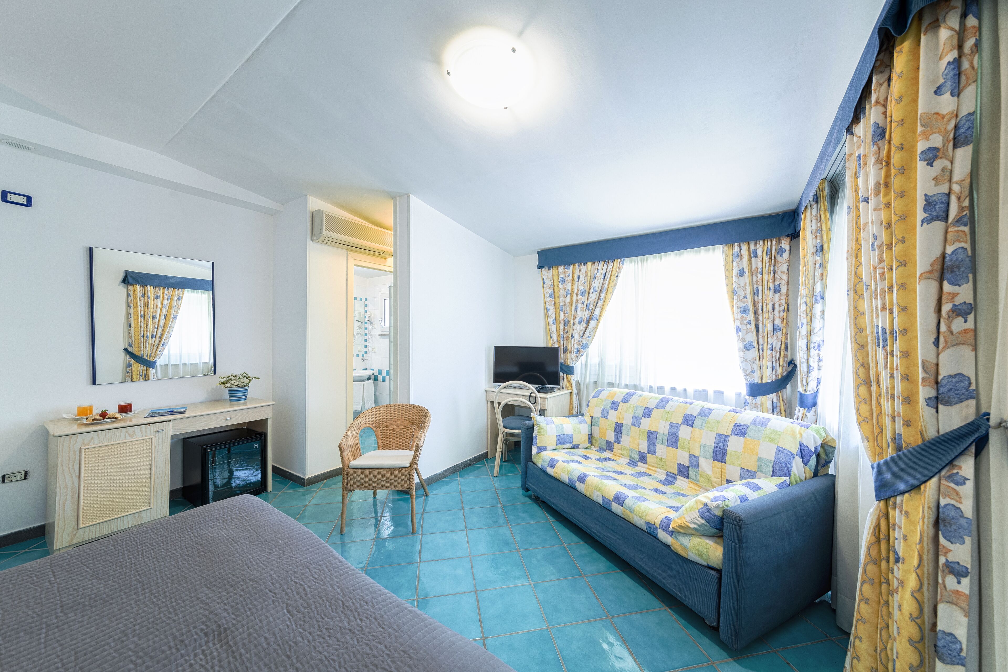 A hotel room with a bed, a desk with a computer, a chair, and a small TV.