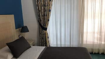 Une chambre d’hôtel avec un lit, une table de chevet, une lampe, une fenêtre avec des rideaux et un mur bleu.