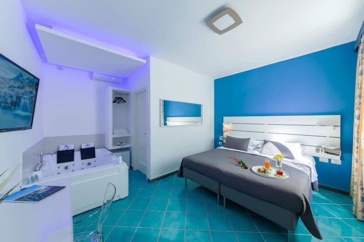 A modern hotel room with a large bed, a vanity with a mirror, and a small seating area.