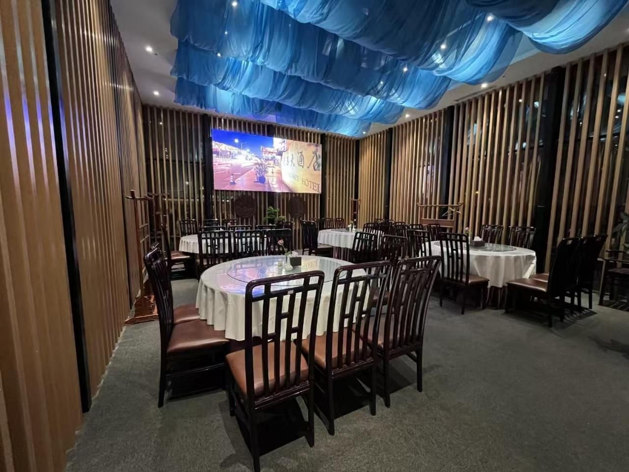 Sala de conferências com mesas e cadeiras redondas, uma tela grande e teto azul.