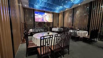 Sala de conferências com mesas e cadeiras redondas, uma tela grande e teto azul.