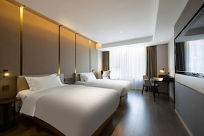 A hotel room with two beds, a desk, and a large window.