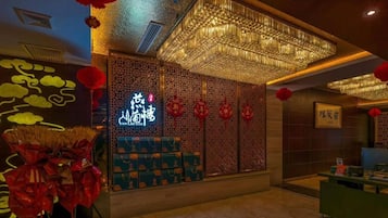 Um saguão de hotel com uma parede decorativa tradicional chinesa, um letreiro de neon e um balcão de recepção.