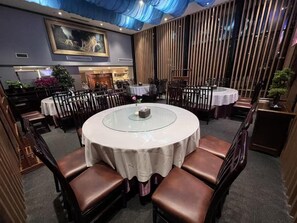 Ein Restaurant mit runden Tischen, braunen Ledersesseln und einem blauen Vorhang darüber.