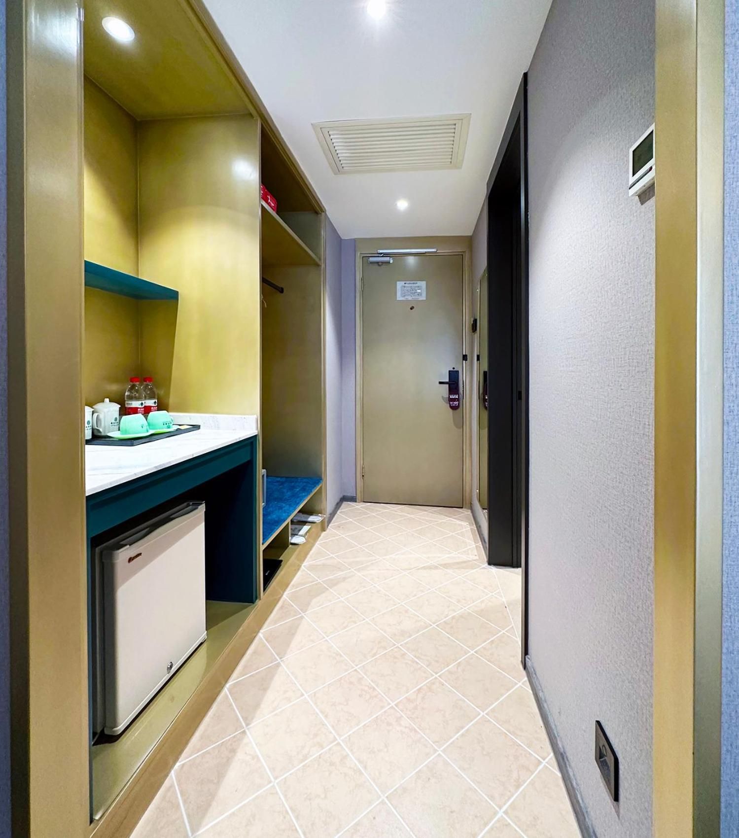 Un couloir étroit, avec un coin cuisine sur la gauche, une porte au fond et un sol carrelé.