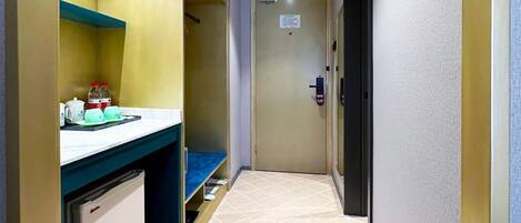 A narrow hallway with a kitchenette area on the left, a door at the end, and a tiled floor.