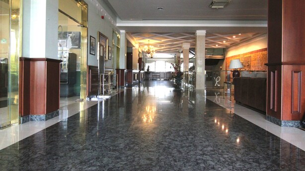 Un vestíbulo amplio con un piso de mármol pulido, grandes columnas y una zona de recepción con mostrador y sillas.
