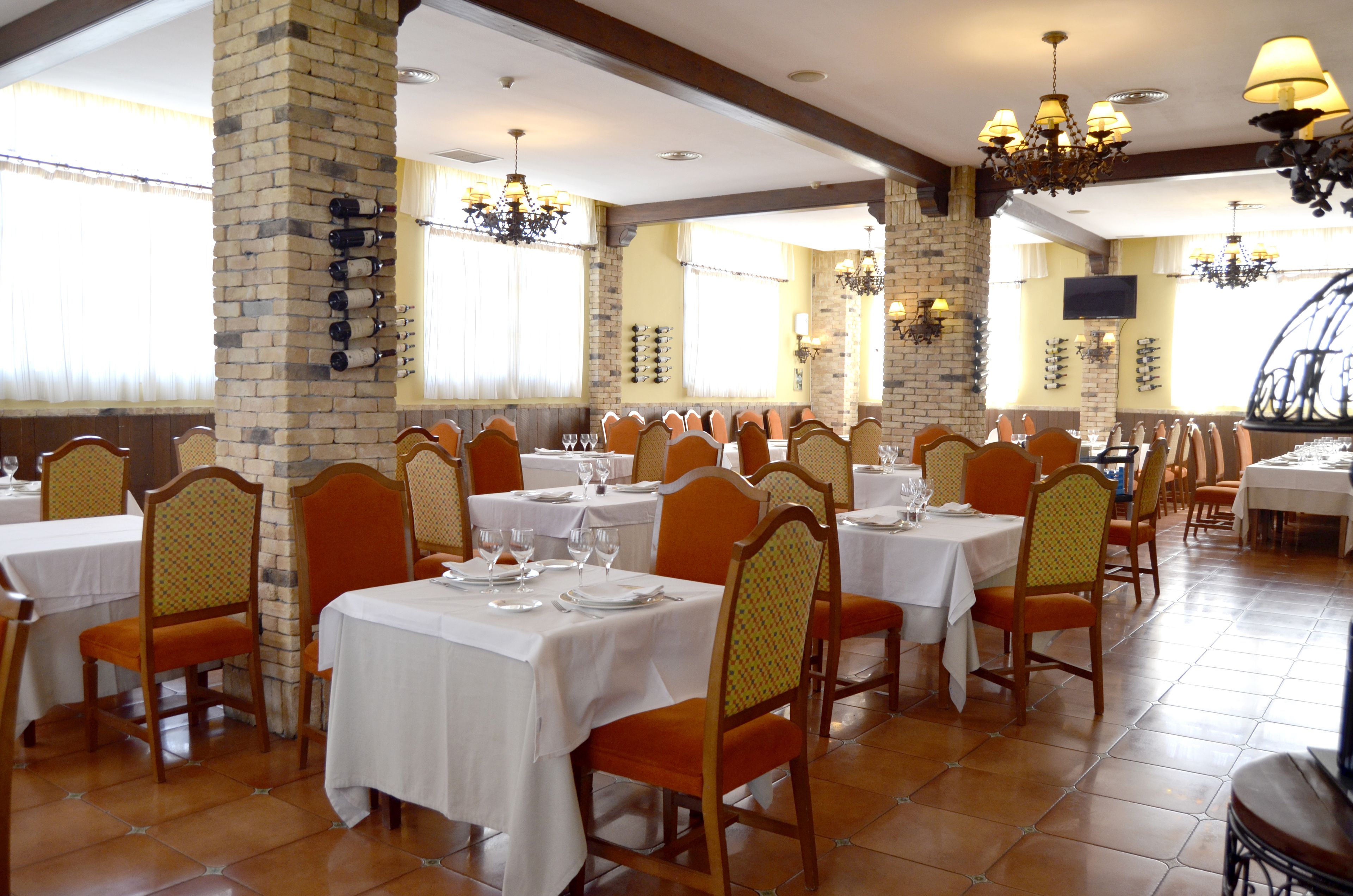 A restaurant with multiple tables and chairs, brick pillars, and chandeliers.
