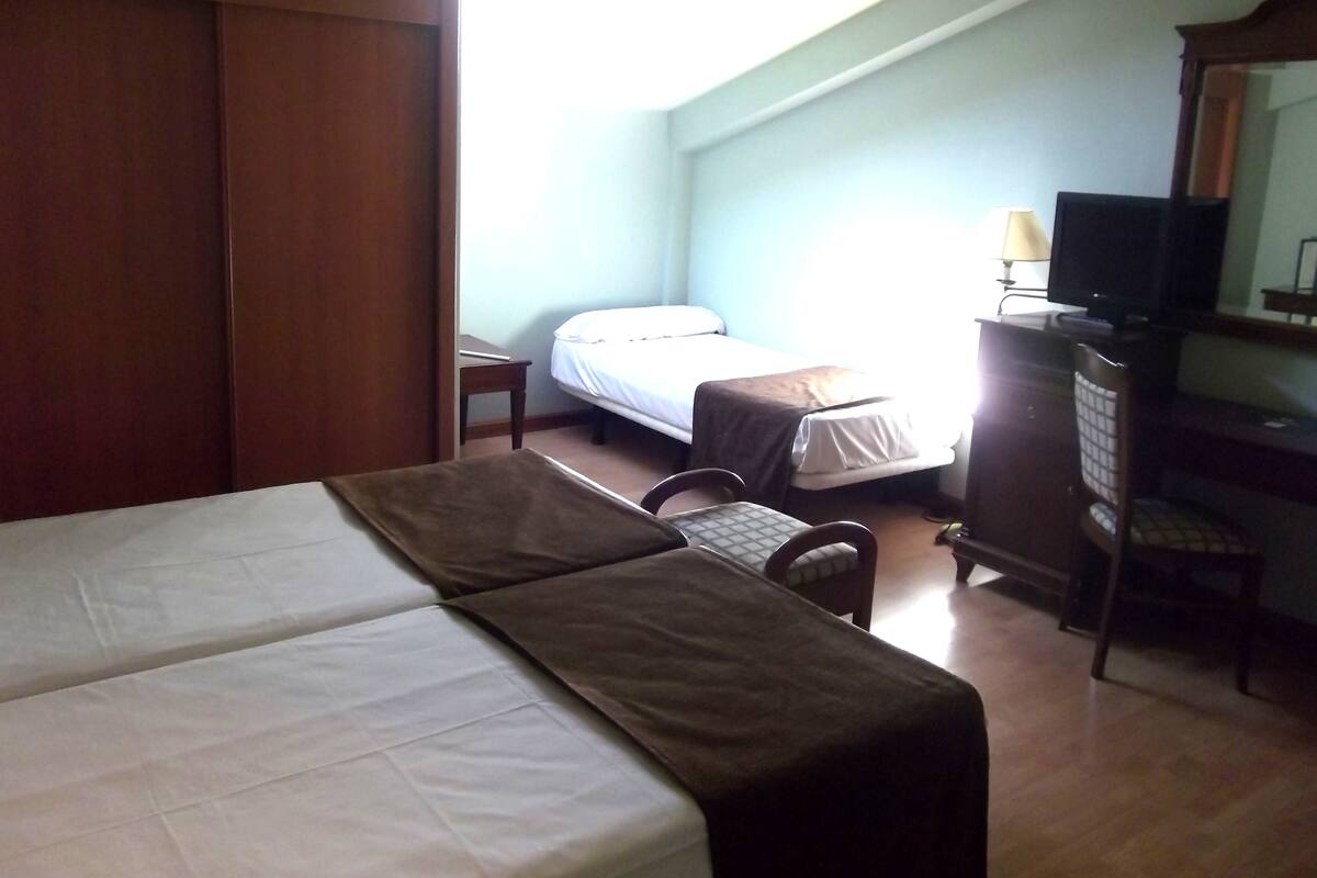 A hotel room with a bed, a desk, a chair, a television, and a wardrobe.