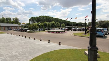 Un estacionamiento con una entrada circular, un edificio de techo rojo y banderas en palos.