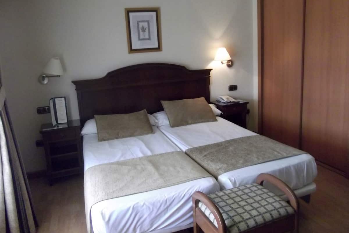 A double bed with two pillows, a bedside table with a lamp, a framed picture on the wall, and a wooden wardrobe.