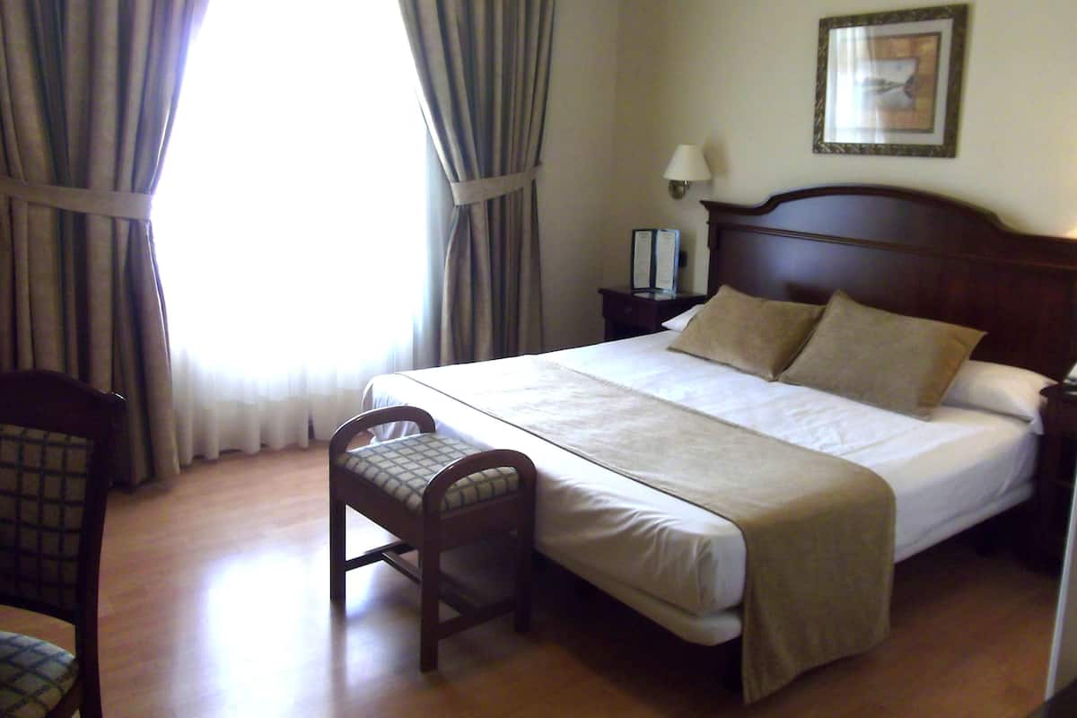 A hotel room with a bed, a chair, a nightstand, a lamp, and a framed picture on the wall.