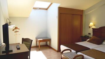 Habitació d'hotel amb un llit individual, escriptori amb cadira, taula petita, làmpada i armari.