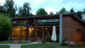 A modern wooden cabin with large glass windows, a patio area with a table and chairs, and a garden with potted plants. - Hotel Río Bidasoa (Hondarribia)