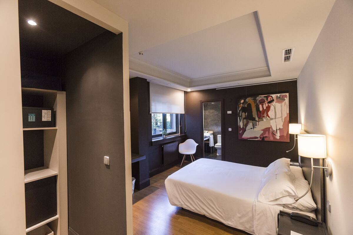 A hotel room with a bed, bedside table, lamp, and a painting on the wall.