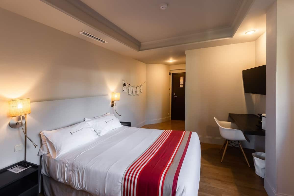 A hotel room with a bed, bedside lamps, a desk, and a chair.