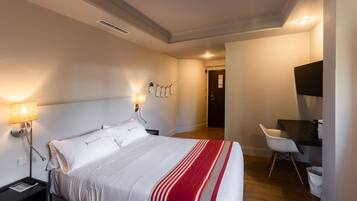 A hotel room with a bed, bedside lamps, a desk, and a chair.
