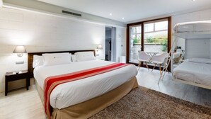 A modern bedroom with a large bed, a small table, two chairs, and a window with a view of greenery. - Hotel Río Bidasoa (Hondarribia)