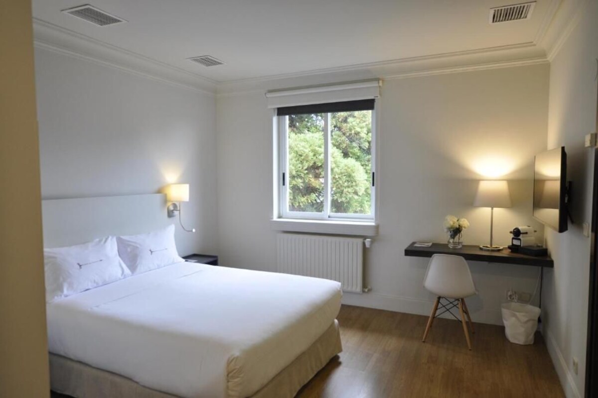 A bedroom with a bed, a desk with a chair, a window, and a radiator.