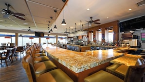 A bar area with a long counter, multiple ceiling fans, and bar stools. - San Vicente Golf Resort (Ramona)