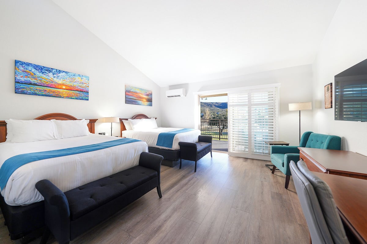 A hotel room with two beds, a sofa, a desk, and a balcony with a view.