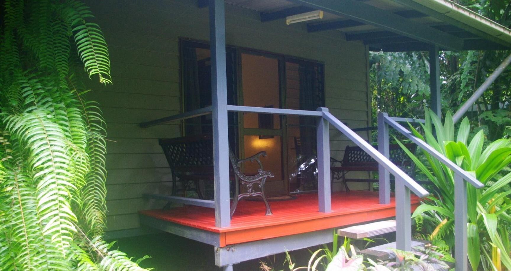 A porch with a red floor, two chairs, and a metal bench.